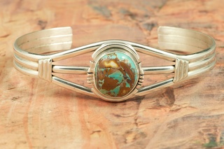 Genuine Boulder Turquoise set in Sterling Silver Bracelet. The cabochon is Boulder Turquoise, you can see the veins of Turquoise running through the host rock. The Boulder Turquoise Mine is located in northeast Nevada. It was discovered in 1970 by a Shoshone sheep herder. Production is small due to the remote location and winter weather. Boulder Turquoise is valued for both it's beauty and rarity. Every stone is unique. Created by Navajo Artist Arkie Nelson. Signed by the artist.